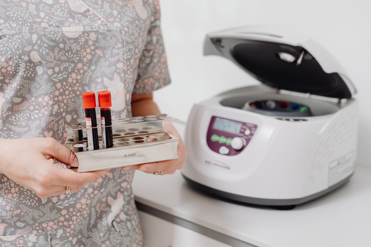 Healthcare professional holding blood vials next to a laboratory centrifuge, indoors.